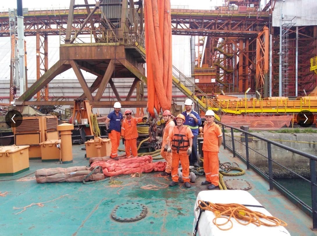 Equipe de rigging prepara cintas e manilhas para içamento junto a guindaste portuário sobre embarcação
