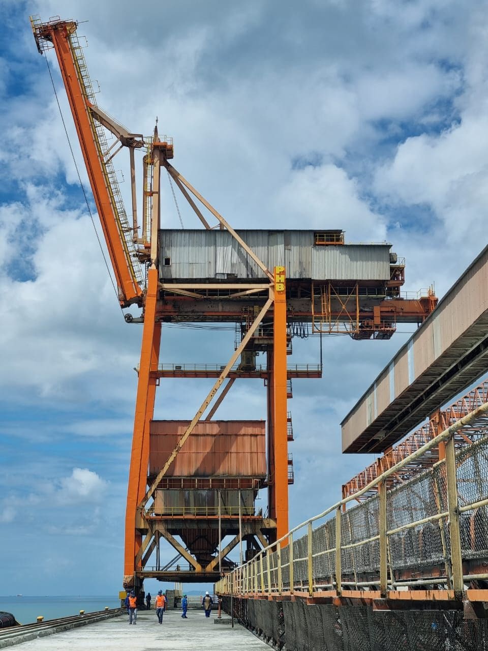 Guindaste portuário com lança elevada junto a correia transportadora no píer de Aratu